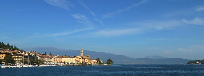 Trip Austria beliebte Urlaubsziele am Gardasee -  Mit einer Fläche von 370 km² ist der Gardasee der größte See Italiens. Es liegt am Fuße der Alpen und erstreckt sich über drei Staaten: Lombardei, Venetien und Trentino. Die maximale Tiefe des Sees beträgt 346 m, er hat eine längliche Form und sein nördliches Ende ist sehr schmal. Dort ist der See von den Bergen der Gruppo di Baldo umgeben. Du trittst aus deinem gemütlichen Hotelzimmer und es begrüßt dich die warme italienische Sonne. Du blickst auf den atemberaubenden Gardasee, der in zahlreichen Blautönen schimmert - von tiefem Dunkelblau bis zu funkelndem Türkis. Majestätische Berge umgeben dich, während die Brise sanft deine Haut streichelt und der Duft von blühenden Zitronenbäumen deine Nase kitzelt. Du schlenderst die malerischen, engen Gassen entlang, vorbei an farbenfrohen, blumengeschmückten Häusern. Vereinzelt unterbricht das fröhliche Lachen der Einheimischen die friedvolle Stille. Du fühlst dich wie in einem Traum, der nicht enden will. Jeder Schritt führt dich zu neuen Entdeckungen und Abenteuern. Du probierst die köstliche italienische Küche mit ihren frischen Zutaten und verführerischen Aromen. Die Sonne geht langsam unter und taucht den Himmel in ein leuchtendes Orange-rot - ein spektakulärer Anblick.